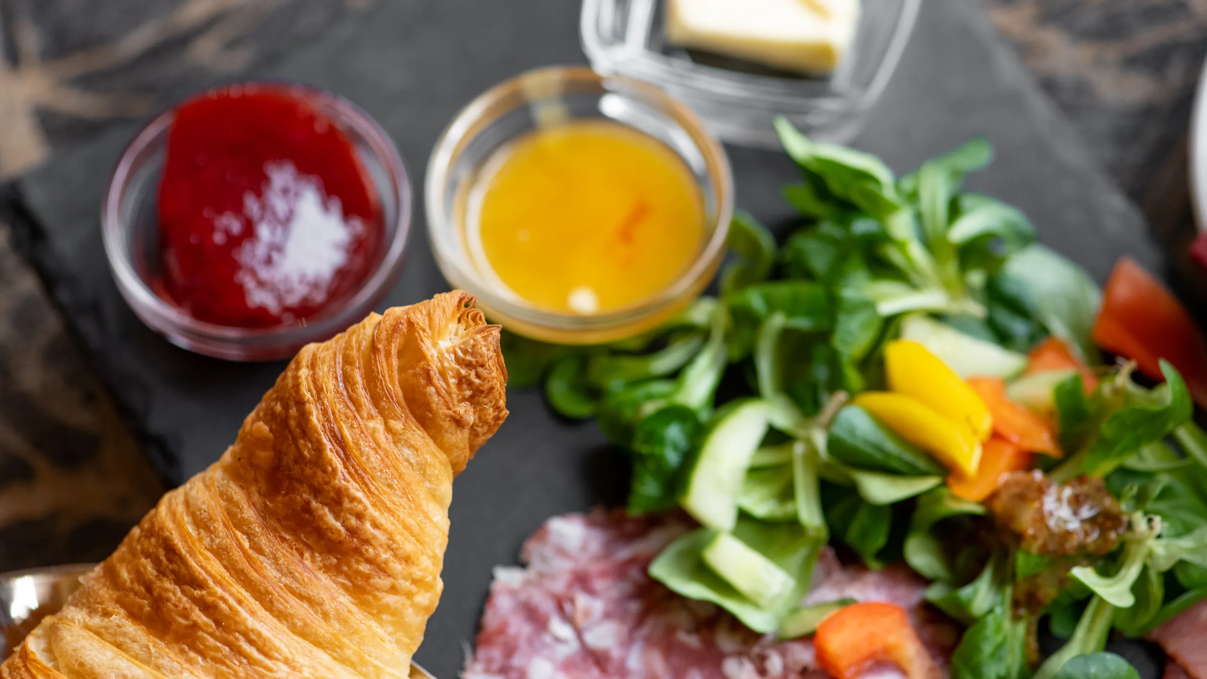 Frühstücksteller mit Croissant, Konfitüre, Salat und Wurst auf Schiefer