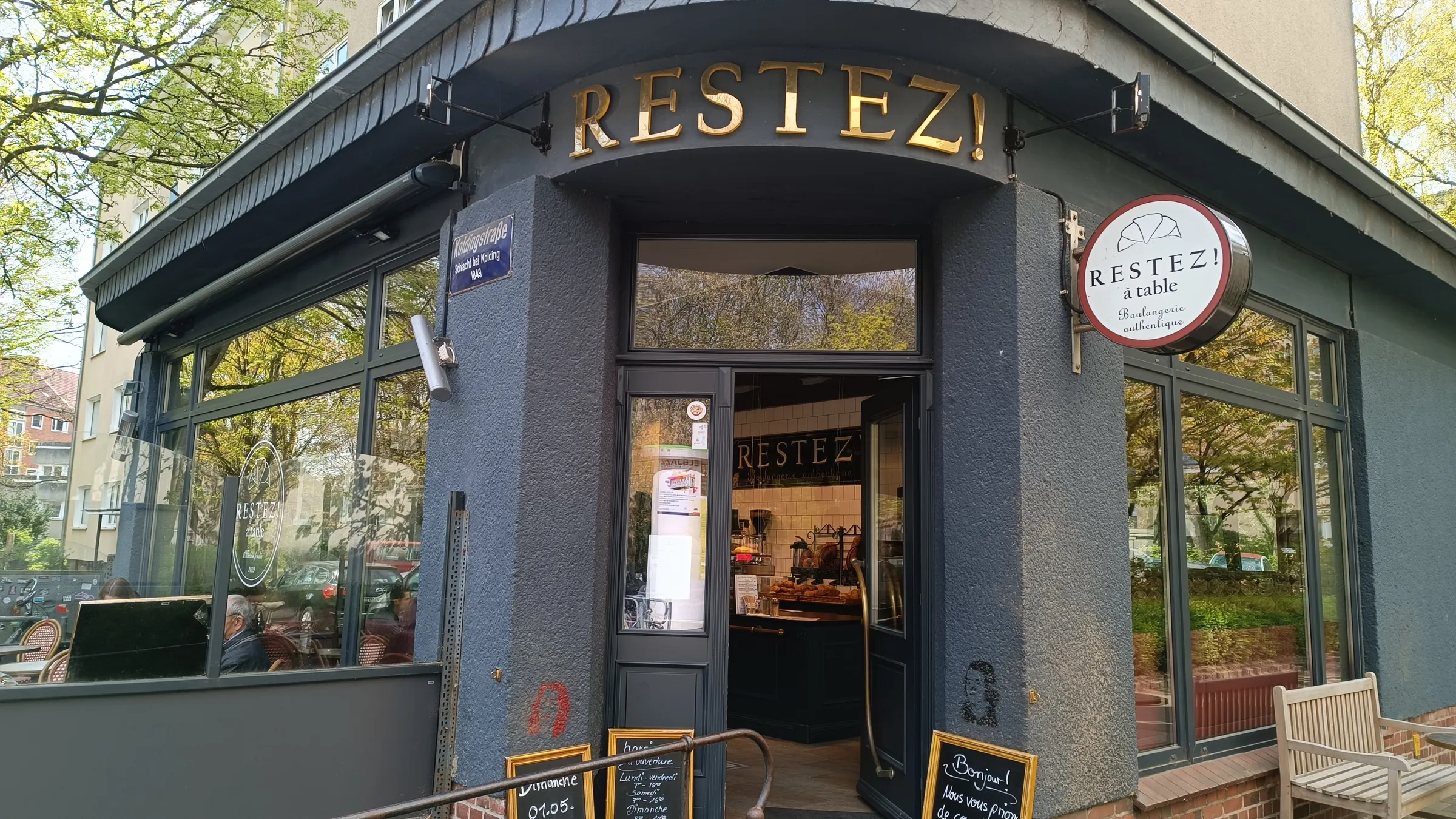 Eingang in der Koldingstraße mit goldenem Schriftzug und dem Rundschild „à table“